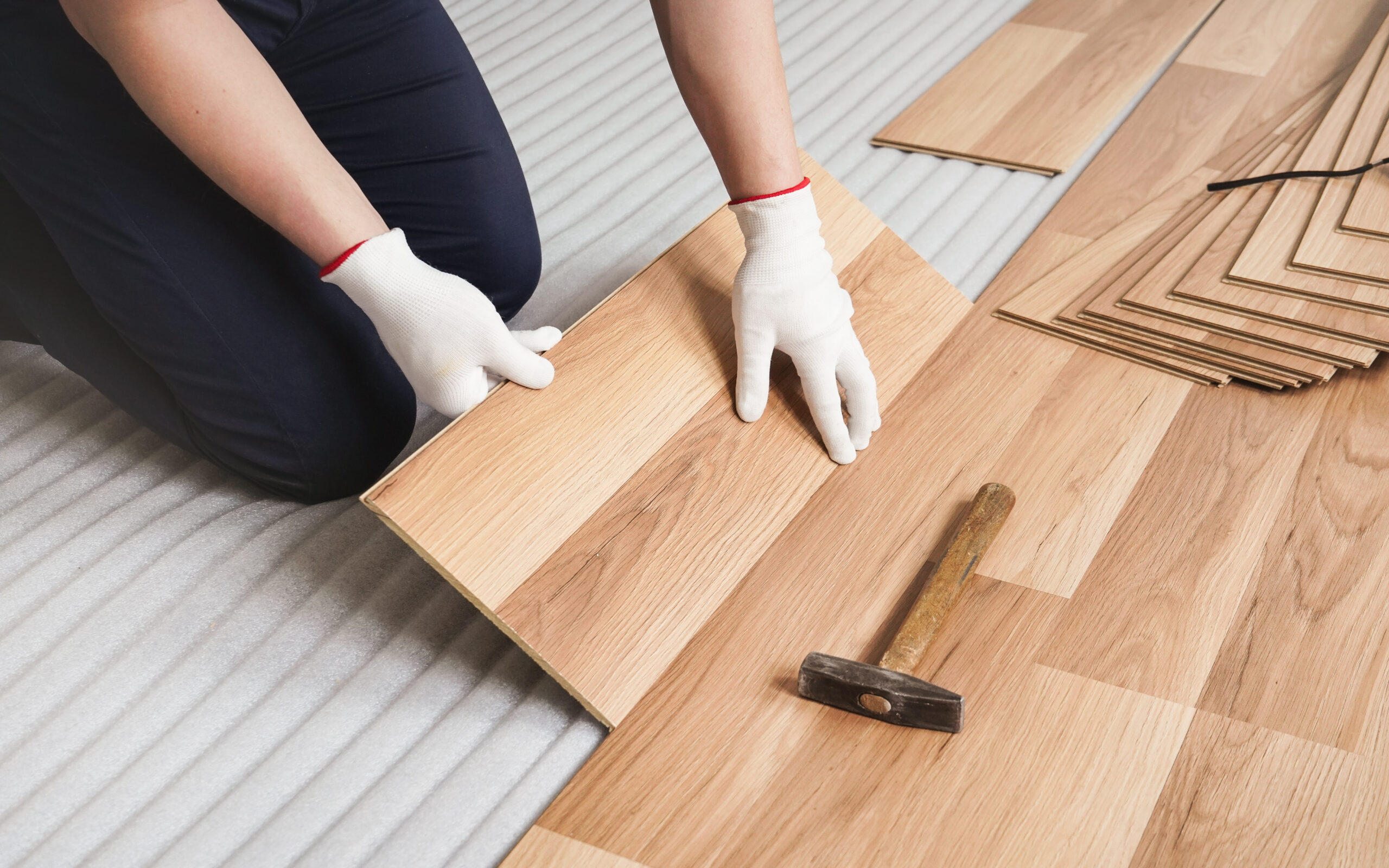 Man installing laminated floor, detail on wooden tile being fitted, over white foam base layer.